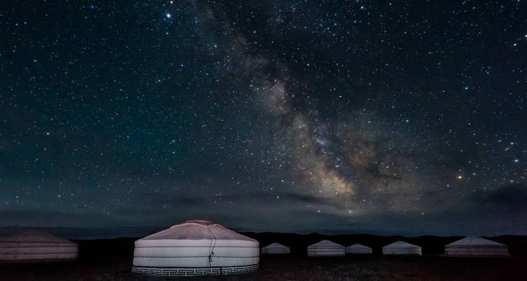 Des yourtes mongoles traditionnelles se dressent sous un ciel dramatique de la Voie lactée rempli d'étoiles dans le désert isolé.