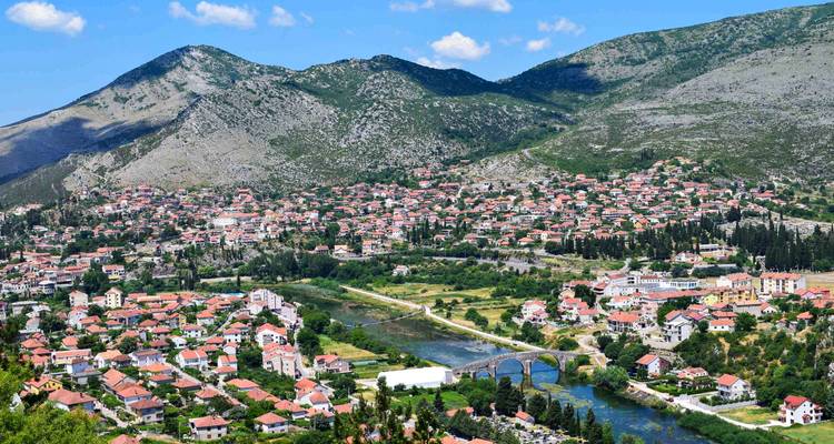 Elevated view of Trebinje town with red-roofed houses nestled between green mountains.