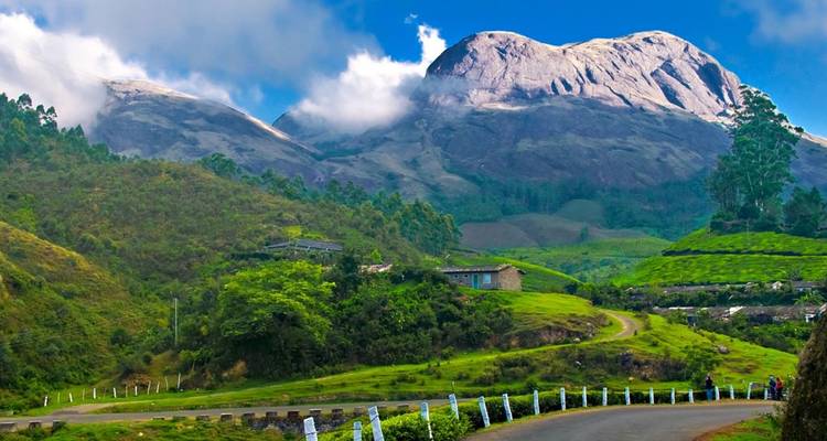 Dramatische bergachtergrond en kronkelende weg door weelderige groene heuvels van Munnar onder vlekkerige wolken.