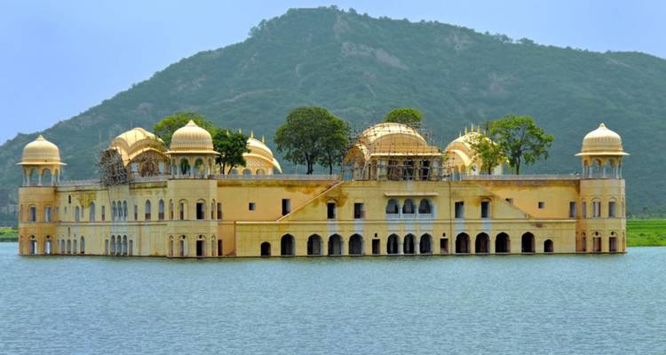 Goldener Jal Mahal Palast schwimmend in der Mitte des Man Sagar Sees mit grüner Hügelkulisse im Hintergrund.