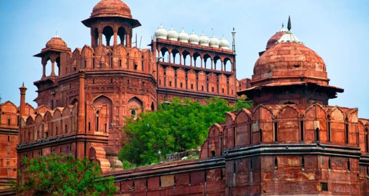 Indrukwekkende rode zandstenen bolwerken en koepels van het Rode Fort tegen een blauwe hemel.
