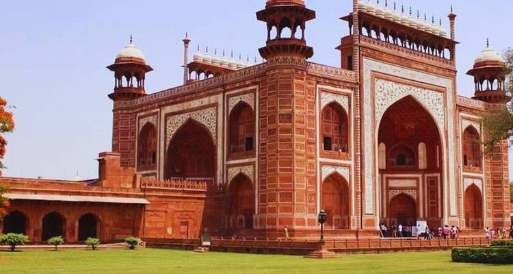 Grand portail en grès rouge du complexe du Taj Mahal sous un ciel dégagé et une pelouse verte
