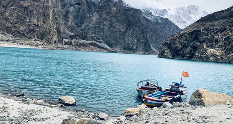 Lago glacial turquesa enmarcado por montañas rocosas empinadas con botes coloridos amarrados