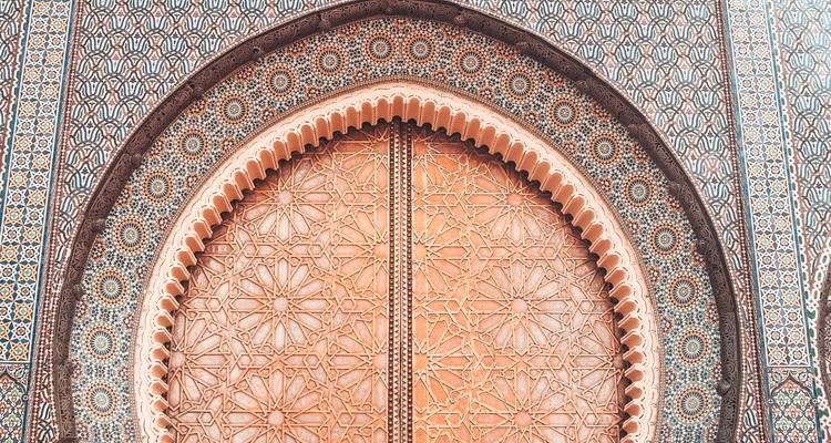 Detailed Moorish mosaic arch and carved wooden door with geometric patterns in warm tones.
