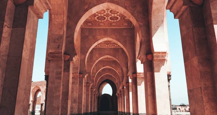 Symmetrical stone arches and patterned ceilings of a mosque’s corridor leading into the distance.