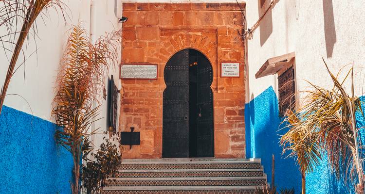 Charming doorway with black arched door, blue-and-white walls and tiled steps in the Kasbah of the Udayas.