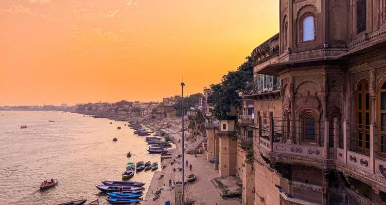 Golden sunset over the Ganges River with historic riverside palaces and boats along the ghats