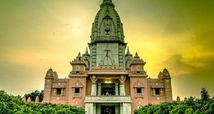 Tall Hindu temple tower rising against a yellow-green evening sky surrounded by greenery