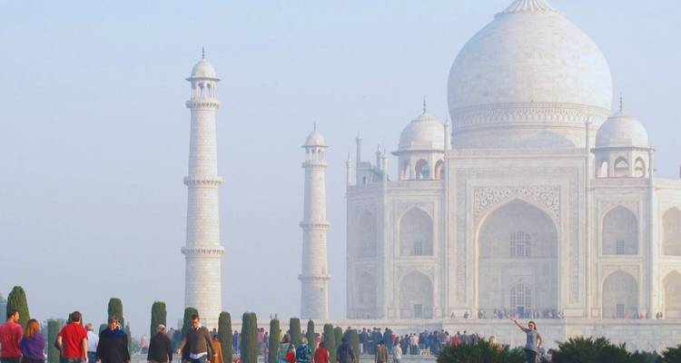 Crowds admire the misty white marble Taj Mahal at dawn with gardens in the foreground