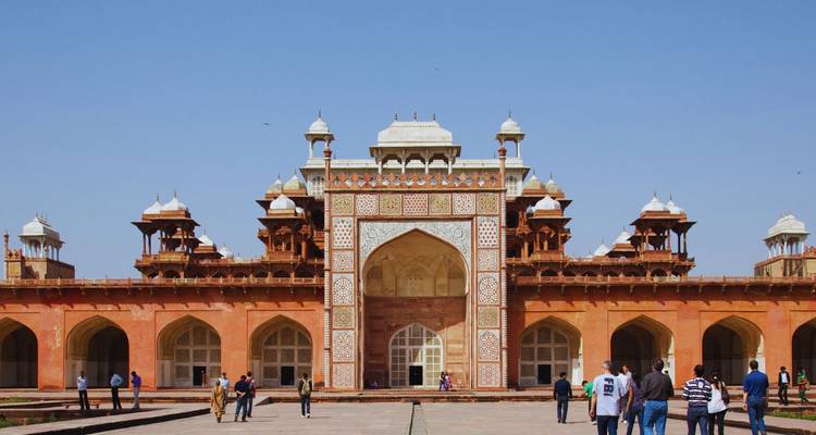 Ornate gateway of Akbar's Tomb complex under a clear blue sky with visitors entering the courtyard