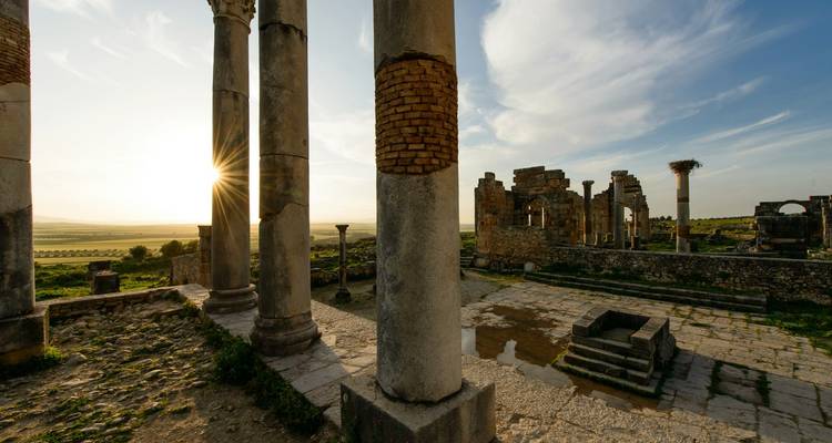 Ancient Roman columns and ruins of Volubilis glow in the low evening sun.