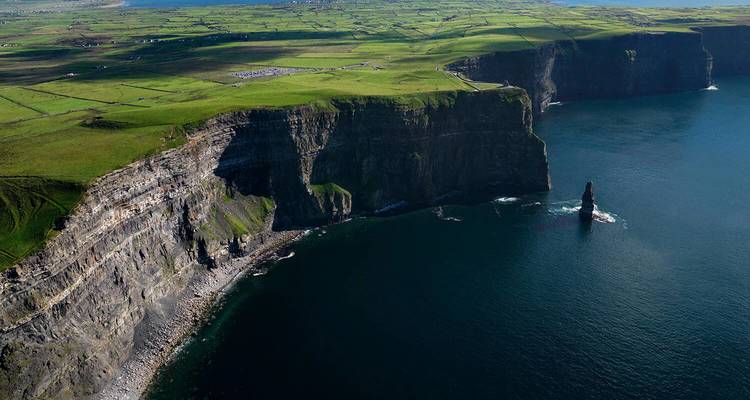 Dramatic aerial of sheer green cliffs dropping vertically into the Atlantic Ocean with sea stack below.