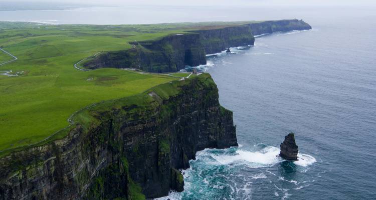 Perspectiva aérea de los escarpados Acantilados de Moher elevándose desde el agitado Atlántico en un día nublado