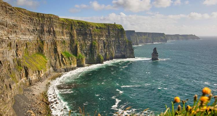 Long stretch of towering sea cliffs battered by waves beneath a bright sky