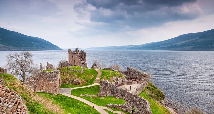 Ruins of Urquhart Castle overlooking expansive Loch Ness under moody skies