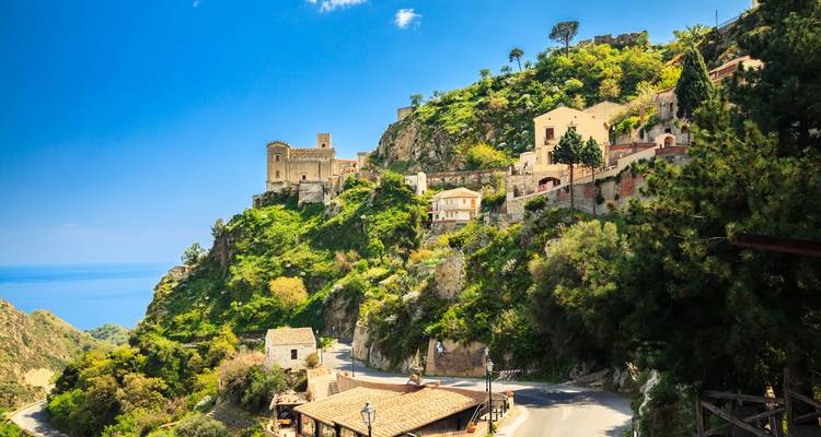 Hilltop medieval village of Savoca with stone church overlooks blue Mediterranean under clear skies.