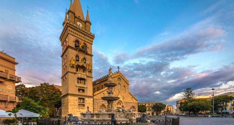Messina Cathedral’s bell tower and fountain highlighted against a colorful early evening sky.
