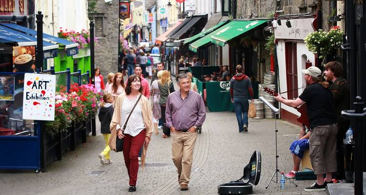 Bustling pedestrian lane in Galway with colorful shopfronts, street musician and flower displays.