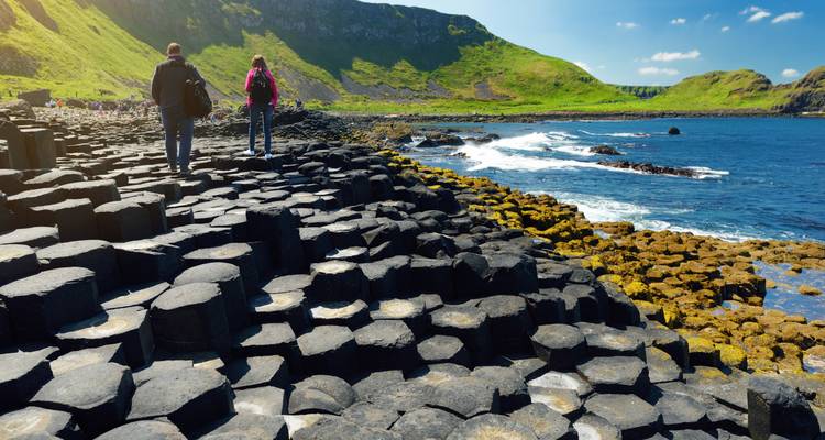 Visitors walking across the hexagonal basalt columns of Giant’s Causeway beside the rugged Atlantic coast.