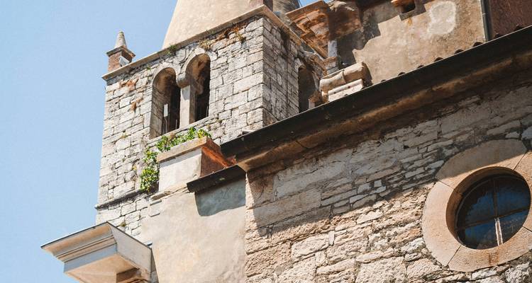 Gros plan du clocher en pierre et de la façade d'église rustique sur un ciel dégagé.
