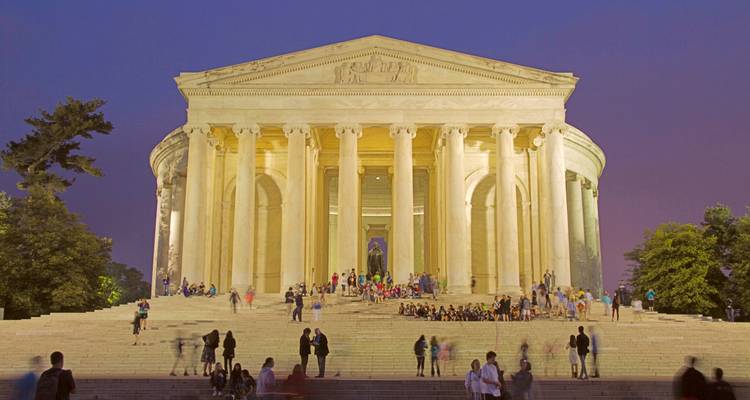 Verlichte Jefferson Memorial in de schemering met bezoekers verzameld op de grote trappen