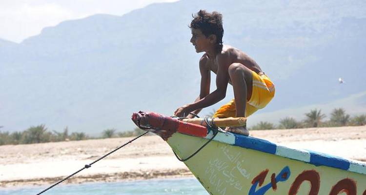 Un niño pequeño se agacha en la proa colorida de un barco de pesca anclado en aguas claras.