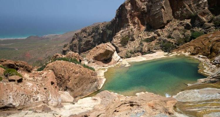 Piscina natural verde aguamarina anidada entre acantilados escarpados en lo alto de la costa de Socotra.