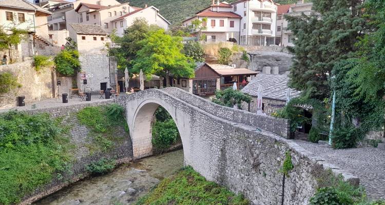 Encantador pequeño puente de arco de piedra que cruza un arroyo poco profundo en un barrio histórico frondoso.