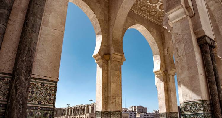Marmeren bogen omlijsten een uitzicht over de binnenplaats van de Hassan II-moskee met blauwe lucht erboven.