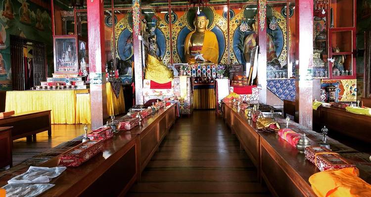 Colorful Buddhist prayer hall with large golden Buddha statue and neatly arranged offerings.