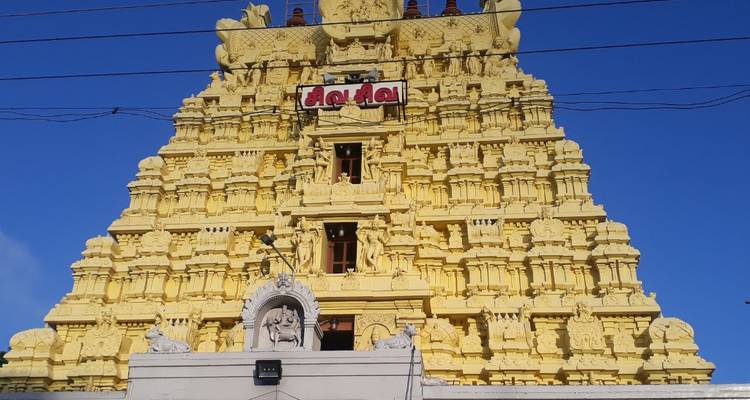 Tour de temple peinte en jaune avec des sculptures complexes se dressant contre un ciel bleu dégagé.