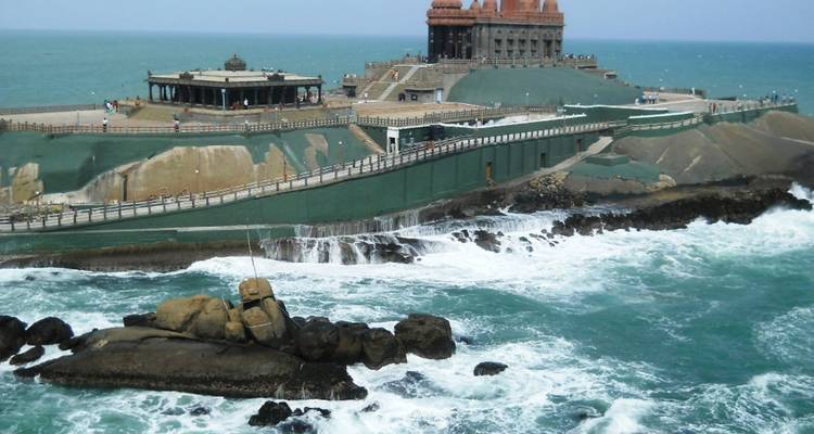 Les vagues de la mer se brisent autour du mémorial de Vivekananda Rock avec une longue chaussée visible.