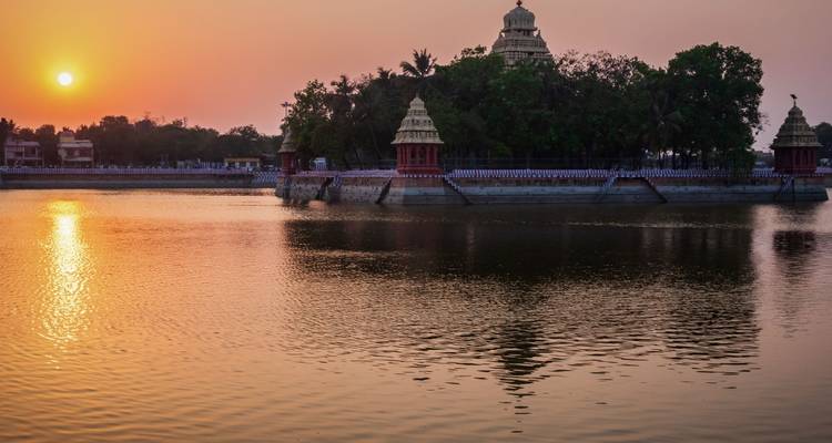 Coucher de soleil doré sur un bassin de temple tranquille reflétant des sanctuaires à coupoles et des arbres.