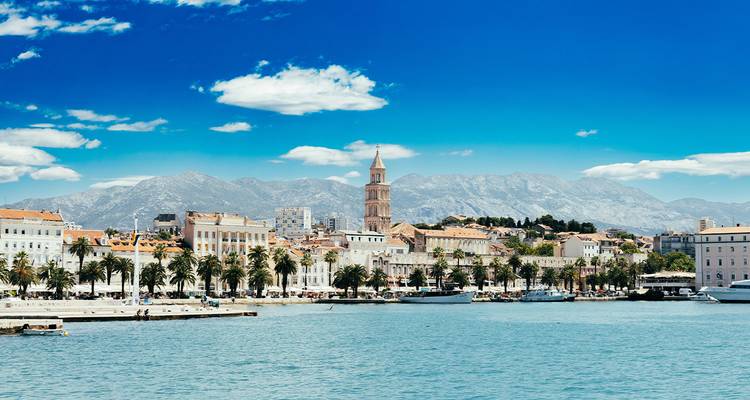 Bord de mer lumineux de Split avec promenade bordée de palmiers, beffroi historique et eau turquoise claire sous un ciel bleu.