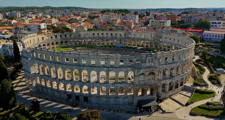 Perspective aérienne de l'ancienne Arène romaine de Pula entourée par les bâtiments modernes de la ville et la végétation.