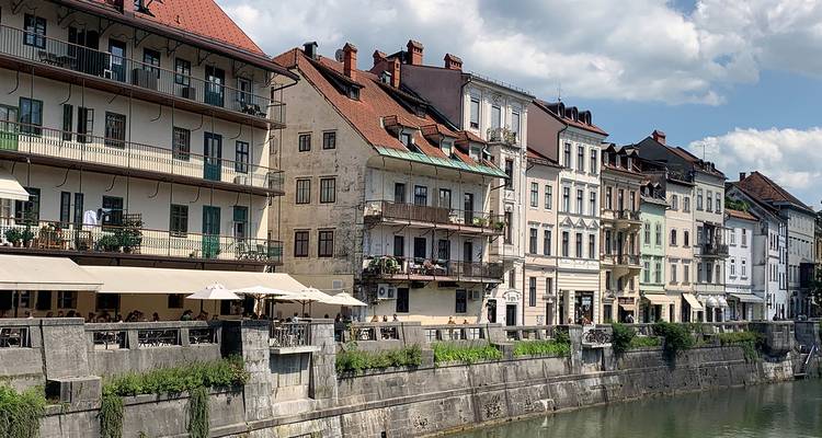 Des bâtiments historiques colorés bordent la rivière Ljubljanica sous des nuages blancs et cotonneux.