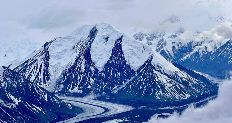Vue aérienne dramatique d'une immense chaîne de montagnes enneigées avec une rivière glaciaire sinueuse en contrebas.