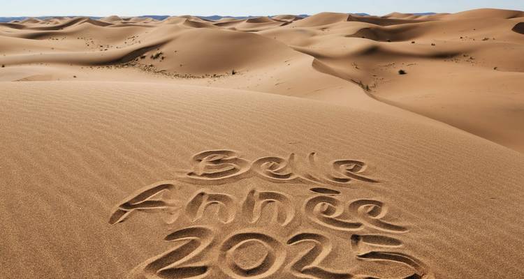 Sweeping sand dunes stretch into the distance with words ‘Belle Année 2025’ written in the foreground sand.