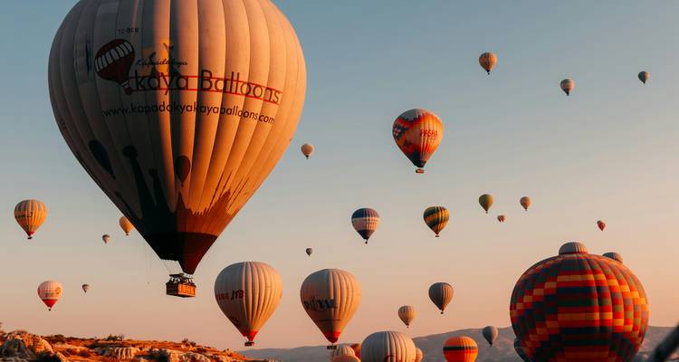 Dozens of colorful hot-air balloons float above Cappadocia’s landscape in the warm light of sunrise.