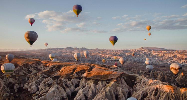Vue aérienne panoramique de dizaines de montgolfières dérivant au-dessus du paysage accidenté de la Cappadoce au lever du soleil.