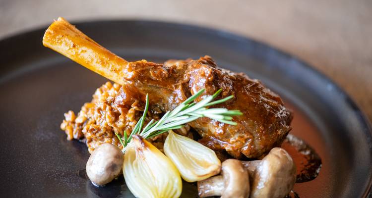 Gourmet lamsbout geserveerd met gestoofde granen, zilveruitjes en champignons gegarneerd met rozemarijn.