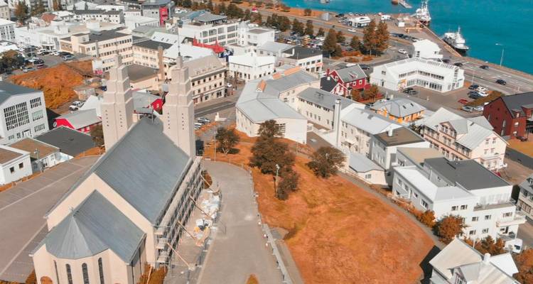 Aerial view over a small Icelandic town dominated by a modern concrete church beside a bright harbour.