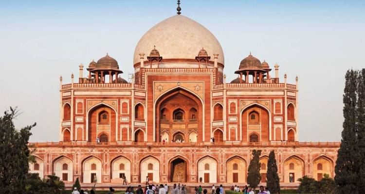 Grand Mughal mausoleum with symmetrical red-and-white facade crowned by a large dome and flanked by lush gardens.