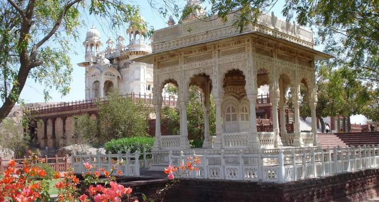Elegant white marble cenotaph and pavilion surrounded by flowering gardens with historic fort in the distance.