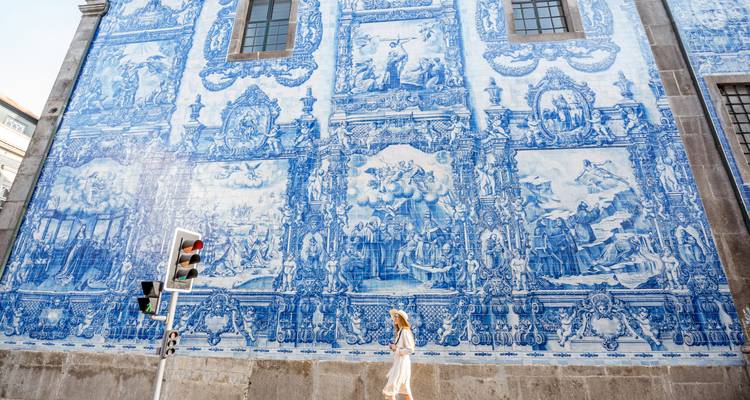 Mujer joven caminando junto al ornamentado mural de azulejos azules de Oporto en una tarde soleada.
