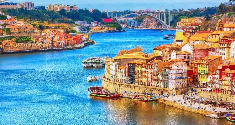 Vibrant panoramic view of Porto’s colourful riverside, traditional boats and Dom Luís I Bridge over the Douro.