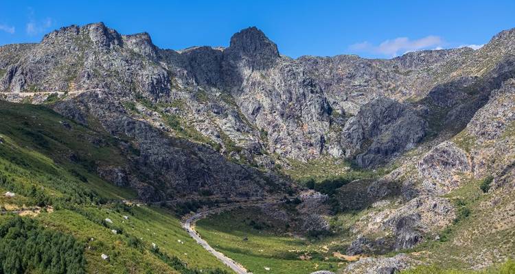 Rocky peaks and deep ravines of Serra da Estrela with a winding mountain road below a blue sky.
