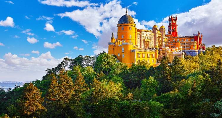 Brightly coloured Pena Palace perched atop a forested hill under a vibrant sky.