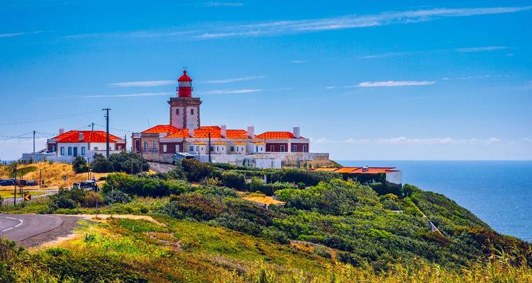 Red-roofed lighthouse complex on a cliff overlooking the Atlantic beneath a bright blue sky.