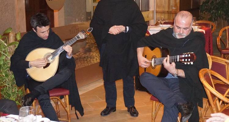 Traditional Fado musicians play Portuguese guitars for diners in an intimate restaurant setting.